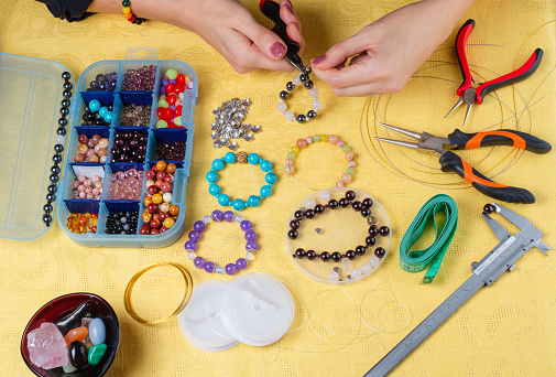Jewelry making. Making a bracelet of colorful beads. Female hands with a tool on a yellow background.