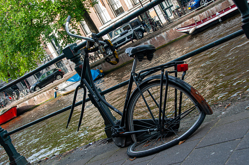 A bent broken bike missing the front wheel and chained to a railing by a canal in Amsterdam during the summer
