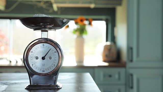 Woman hand's putting flour on an antique scale on the kitchen counter
