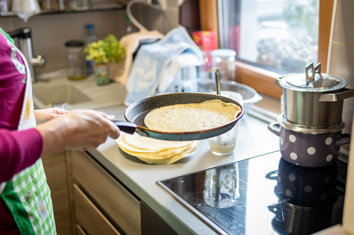 Mature woman making pancakes in the kitchen of her apartment