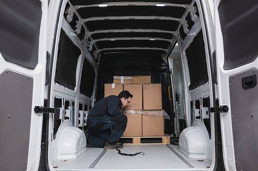 Man picking up boxes in to his cargo van. View from the car trunk. Close-up Of delivery man carrying box.  Rear view of cargo van.