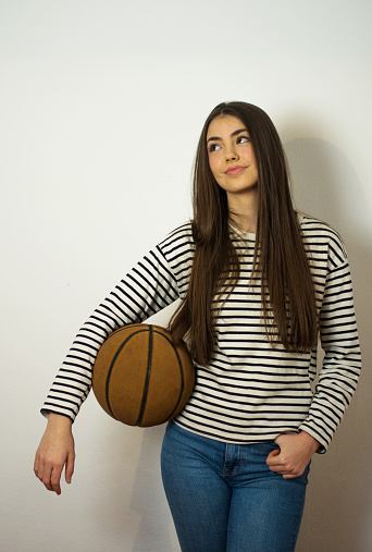 Portrait of young charming woman holding basketball ball while standing against gray background