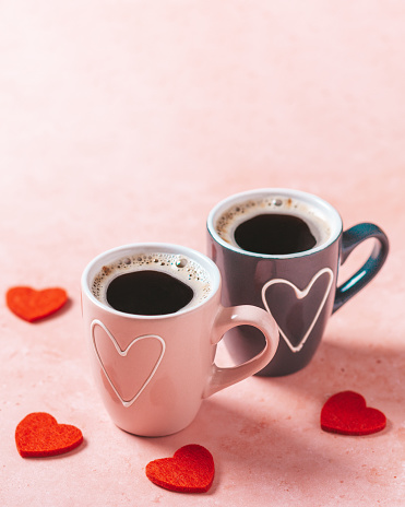 Two coffee cups with heart in pink and black colors standing for female and male gender on pink table with red hearts around, top view. Valentines Day holiday