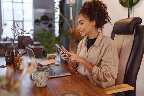 istock Smiling female florist working on laptop in floral studio, using phone for check customers order 1463145083