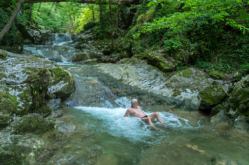 Senior men refreshing himself and relaxing in rapid of cold river in forest at Šmarjetske toplice - spa