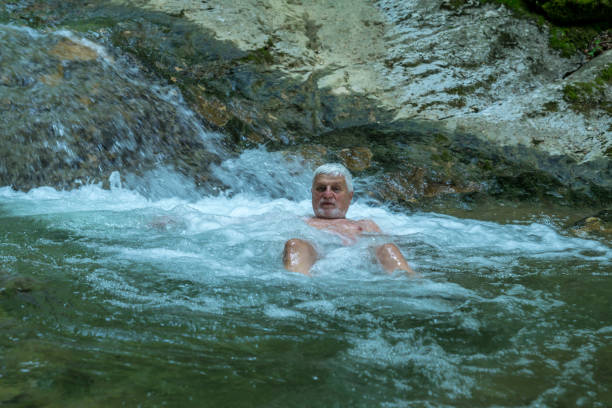 Senior men refreshing himself and relaxing in rapid of cold river in forest at Šmarjetske toplice - spa