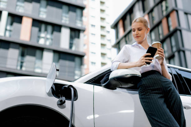 Focus progressive woman using phone and holding coffee at charging station.