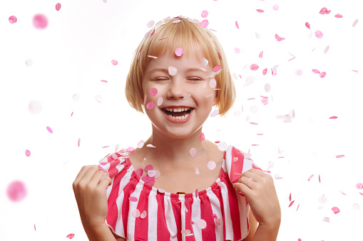A girl in a festive dress on a spruce background laughs, confetti fly around. Concept for birthday party, greeting cards and holiday social media posts.