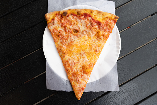 An overhead view of a simple slice of New York City style cheese pizza on a white paper plate