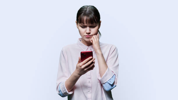 Serious young female using smartphone for typing, reading, on blue background