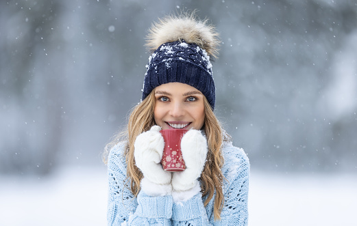Beautiful smiling young woman in warm clothing with cup of hot tea coffee or punch.