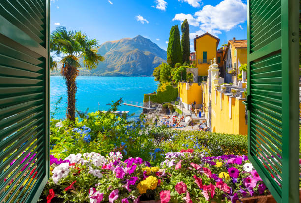 View through an open window with shutters looking down on the colorful picturesque village of Varenna, Italy, on the shores of Lake Como at summer. View through an open window with shutters looking down on the blue water and colorful picturesque resort village of Varenna, Italy, on the shores of Lake Como at summer. como italy stock pictures, royalty-free photos & images