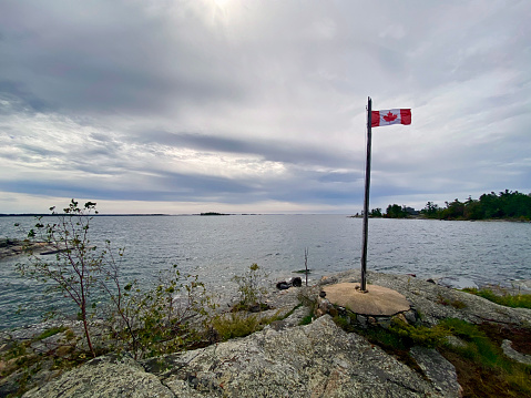 The Canadian flag flying on a rocky shoreline on the edge of Georgian Bay