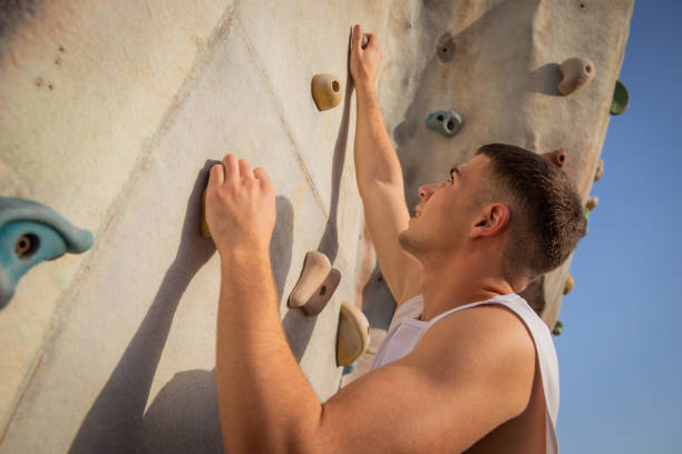 View from behind of a little Caucasian girl climbing a training wall outdoors, being physically active and not giving up
