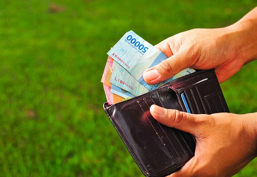 a man's hand taking out Indonesian money from a wallet with blur background