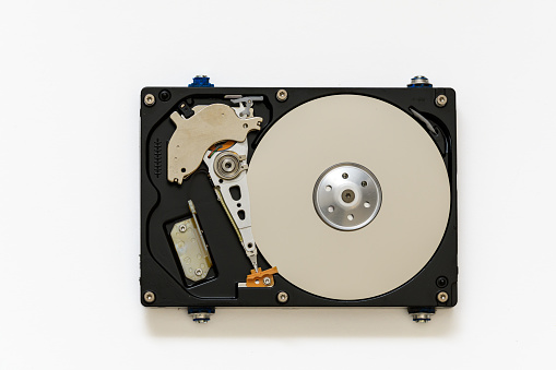 Disassembled computer hard drive. You can see all the electronic and mechanical parts of the hard drive, on a white background.