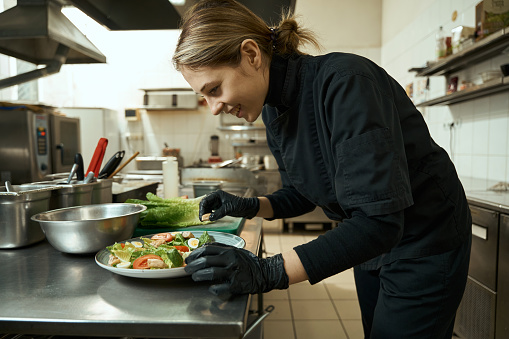 Smiling female chef in a restaurant kitchen decorates a plate with salad, this is a dietary, low-calorie dish