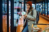 Young woman buying dairy product and reading food label in grocery store.