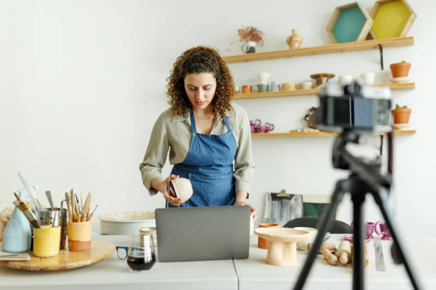 istock Females potter making a vlog, recording online course, lessons in her studion with earthenware shelf on background 1463253853