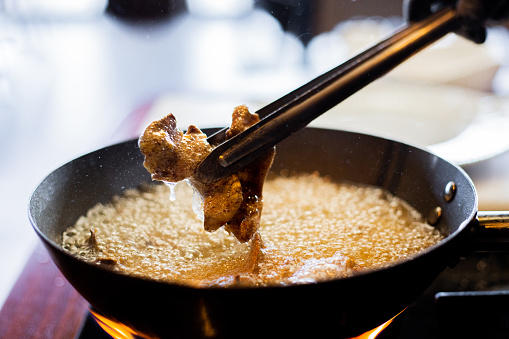 Pieces of meat fried in hot oil are removed from the pan with the help of tongs.