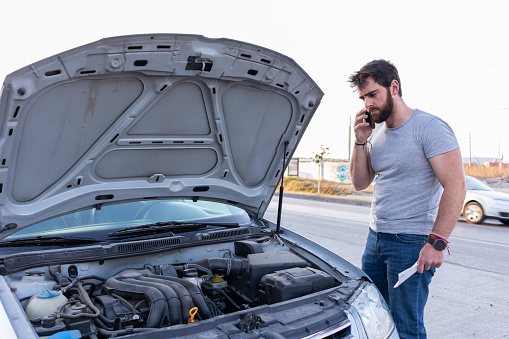 good looking guy, frustrated looking at car's motor with opened hood, having trouble on the road