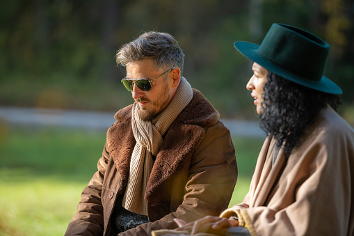 A young Latino woman and a white man are having a friendly conversation. A man with sunglasses, a woman with a green hat and a poncho. Autumn.