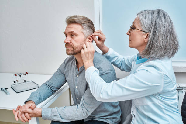 istock Experienced female doctor fitting Intra-The-Ear hearing aid into patient's ear while consultation in audiology clinic. ITE and ITC hearing aids 1463269629