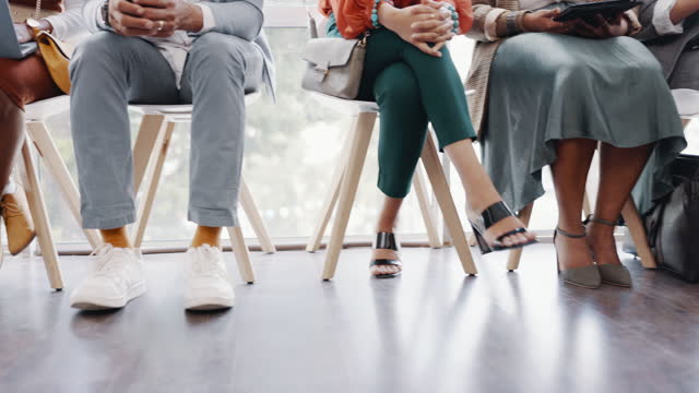 Interview, hiring and legs of business people waiting in a line in the lobby at a modern office. Recruitment, human resources and corporate candidates sitting in a row for a meeting in the workplace.
