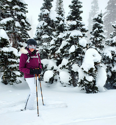 Senior woman skier standing in powder and trees. Powder Mountain ski resort, Utah.