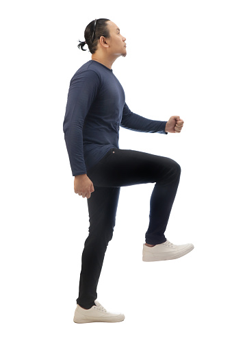 Man wearing casual blue shirt black denim and white shoes, looking up forward and stepping high, side view climbing stair gesture. Full body portrait isolated cut out