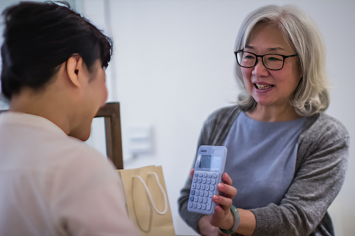 Smiling saleswoman showing calculator with sum for big order to a woman