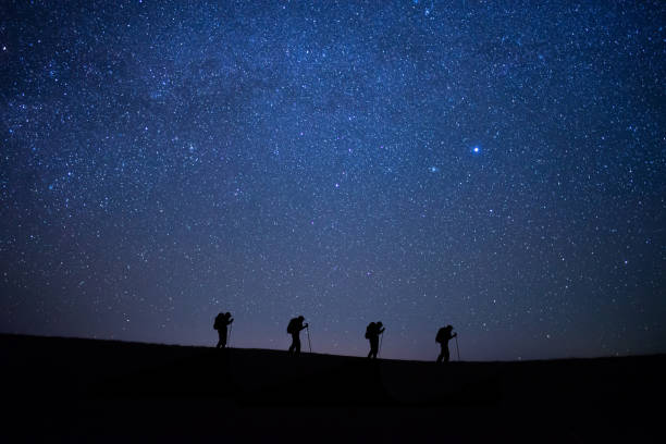 Silhouette small group of young traveler hiking to the top of the mountain with beautiful view star, milky way over the sky. He enjoyed traveling and was successful when he reached the summit. stock photo