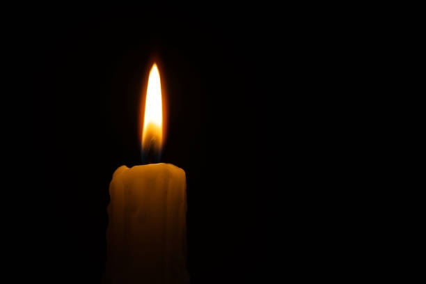 Single burning wax candle against a black background stock photo