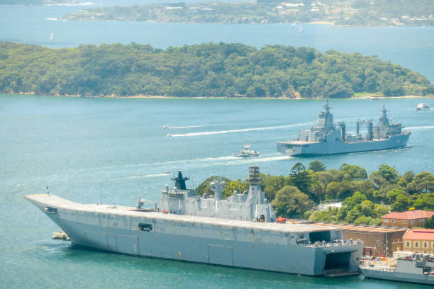 HMAS Supply Departs Sydney Harbour HMAS Supply of the Royal Australian Navy departs Garden Island and prepares to sail out of Sydney Harbour.  She sails past HMAS Adelaide (left) and HMAS Warramunga (right).  She is assisted by two tugboats. The headland jutting out into the harbour is Bradleys Head.  North Head and the harbour entrance are visible at the top left.  This image was taken from Level 29 of Chifley Tower in the afternoon of 6 February 2023. australian navy stock pictures, royalty-free photos & images