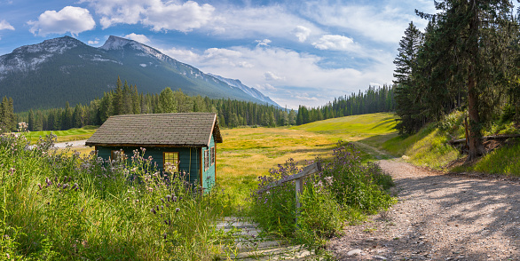Old wooden cabin shelter and beautiful rocky mountain landscape Banff panorama background. Wood building Banff golf course and grassy valley panoramic.