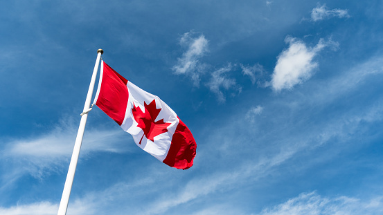 Canada flag pole waving in the wind under beautiful blue sky and clouds wallpaper. Canadian national red maple leaf symbol.