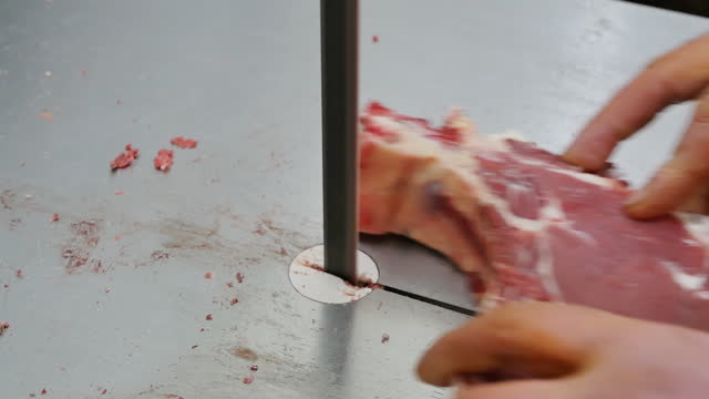Butcher's hands sawing meat and bones on an industrial band electric saw with a vertical cutting blade. Sawing meat carcasses with a special professional saw into parts and pieces