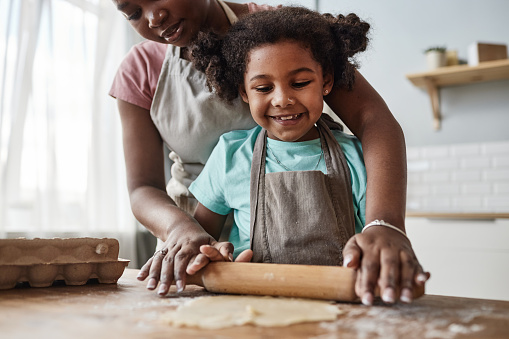 Closeup portrait of loving mother and daughter baking together at home and rolling dough, copy space