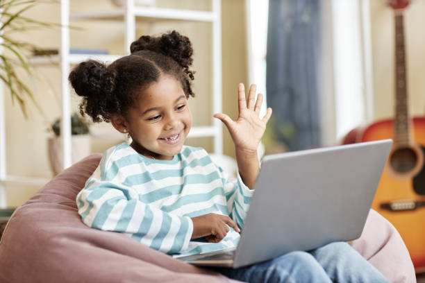 Little black girl waving to laptop camera and smiling