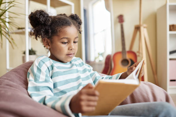 istock Little black girl reading book at home 1463319600