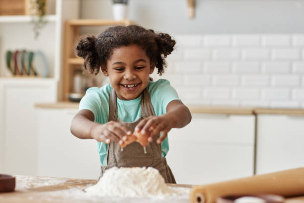 istock Happy little girl baking in kitchen and breaking eggs in flour making dough 1463319630