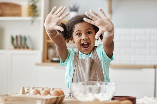 Portrait of happy black girl enjoying baking in kitchen and showing hands with flour to camera, copy space