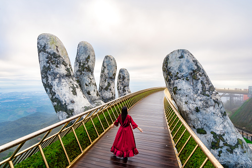 Young woman traveler in red dress enjoying at Golden Bridge in Bana hills, Danang Vietnam, Travel lifestyle concept