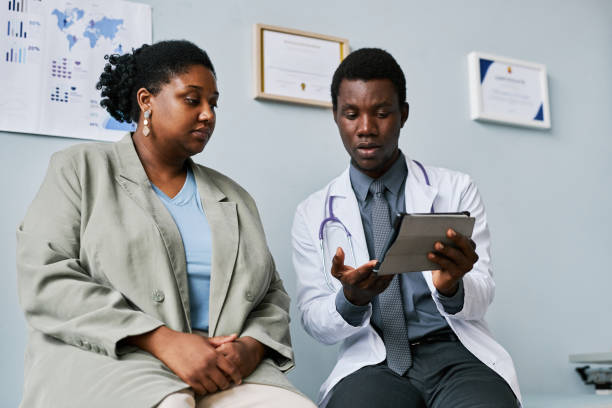 istock Low angle young black doctor patient talking in clinic looking at tablet screen 1463319931