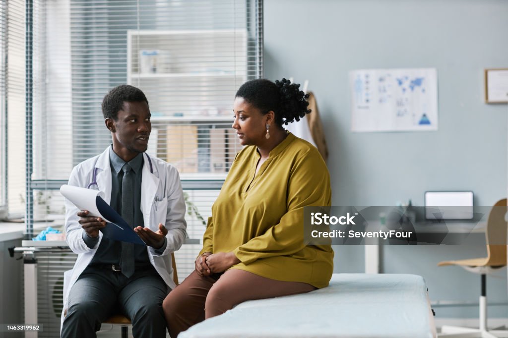 Overweight black woman talking to doctor in medical clinic Side view portrait of overweight black woman talking to doctor in medical clinic, copy space Doctor Stock Photo
