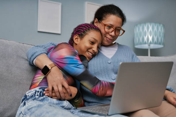 Mother and daughter using laptop together Portrait of black teenage girl using laptop while cuddling with mom on couch preadolescents stock pictures, royalty-free photos & images