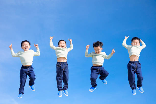 Happy laughing five year old boy jumping outdoors on trampoline, clear blue sky on sunny day