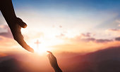 Silhouettes of hands reaching out for hope and supporting each other on sunset background.