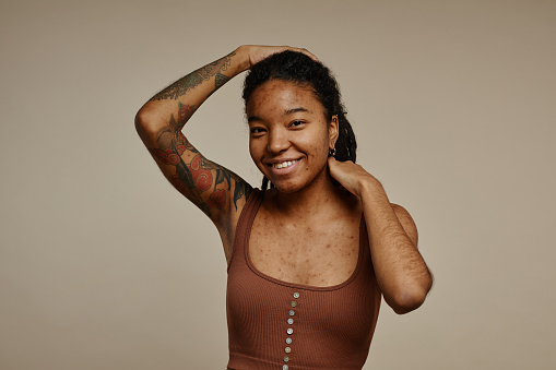 Candid portrait of ethnic young woman with tattoos looking at camera against neutral beige background, copy space
