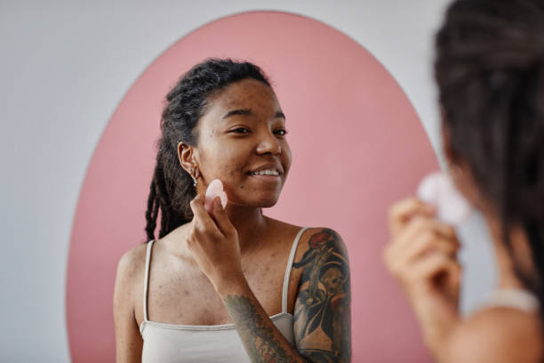 Young black woman with acne scars using face massager during beauty routine